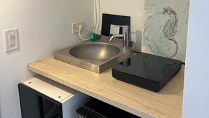 Une cuisine compacte équipée d’un évier, d’un four à micro-ondes, d’un lave-vaisselle et d’une étagère où sont rangées la vaisselle et les tasses.