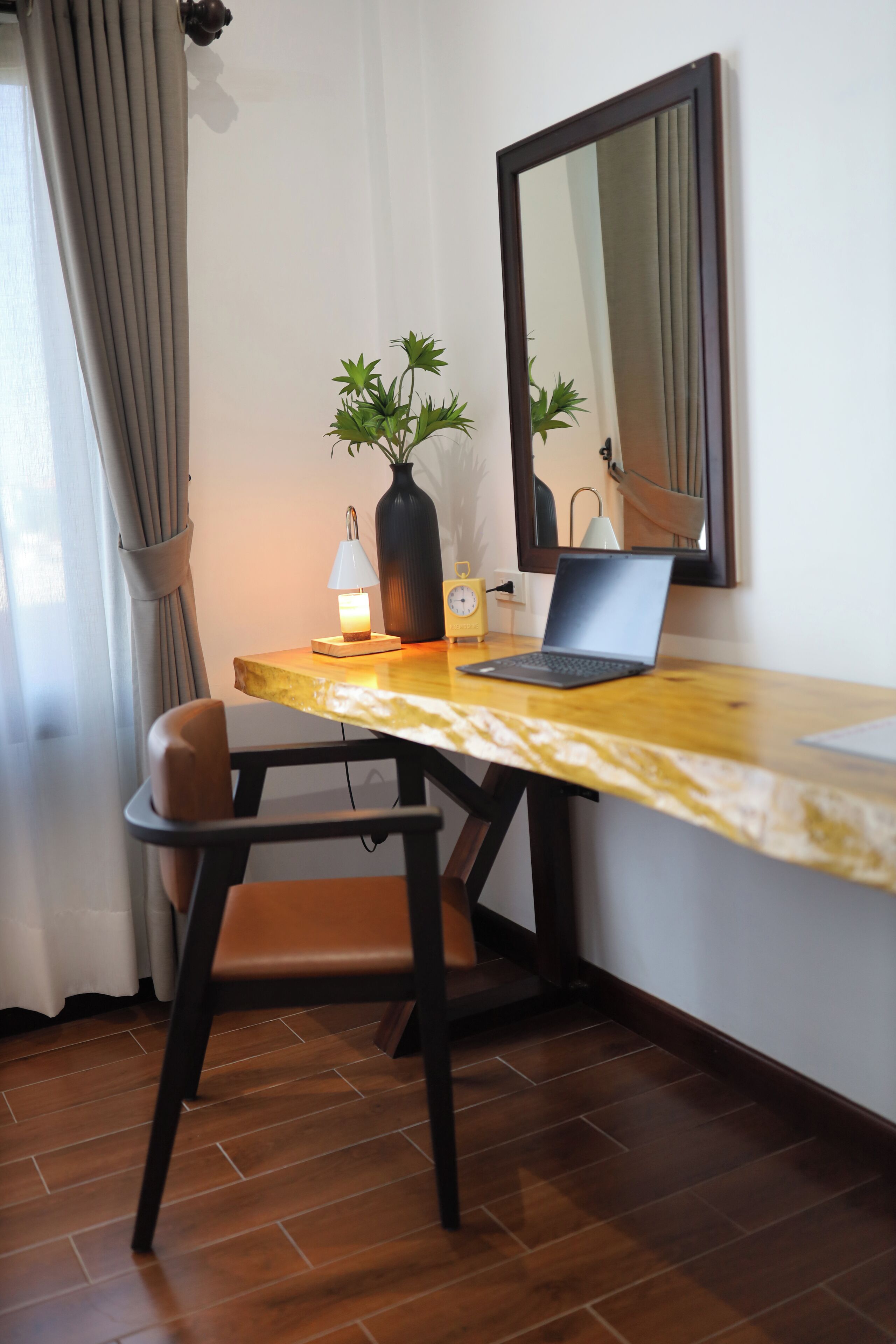 Ein Holztisch mit einem Laptop, einer Pflanzvase, einer Lampe und einer Uhr.