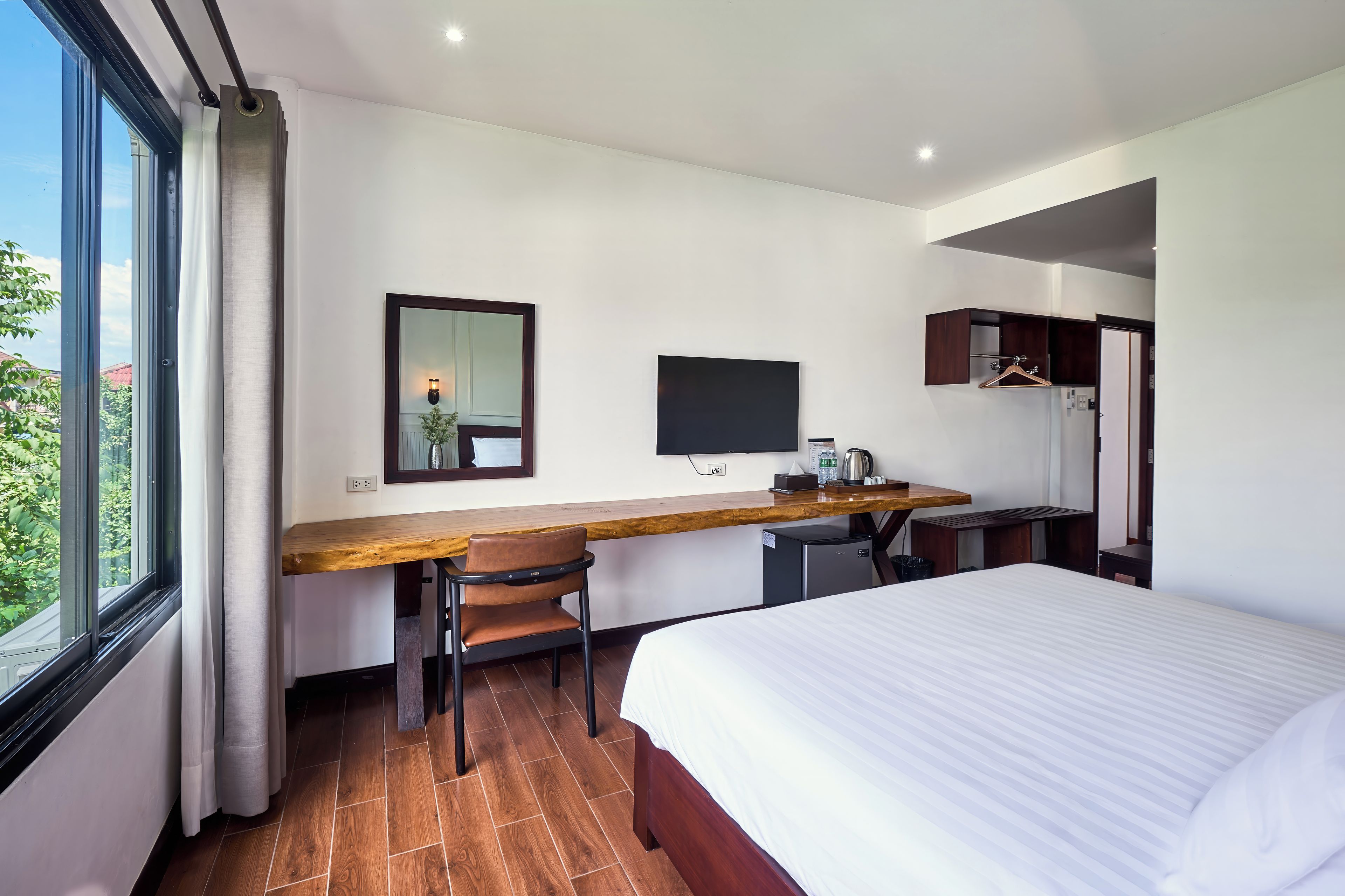 A hotel room with a bed, a desk with a chair, a television, and a wardrobe.