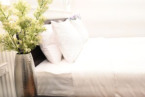 A bed with white bedding, a vase with flowers, and a white wall. - RS1 Hotel (Vientiane)
