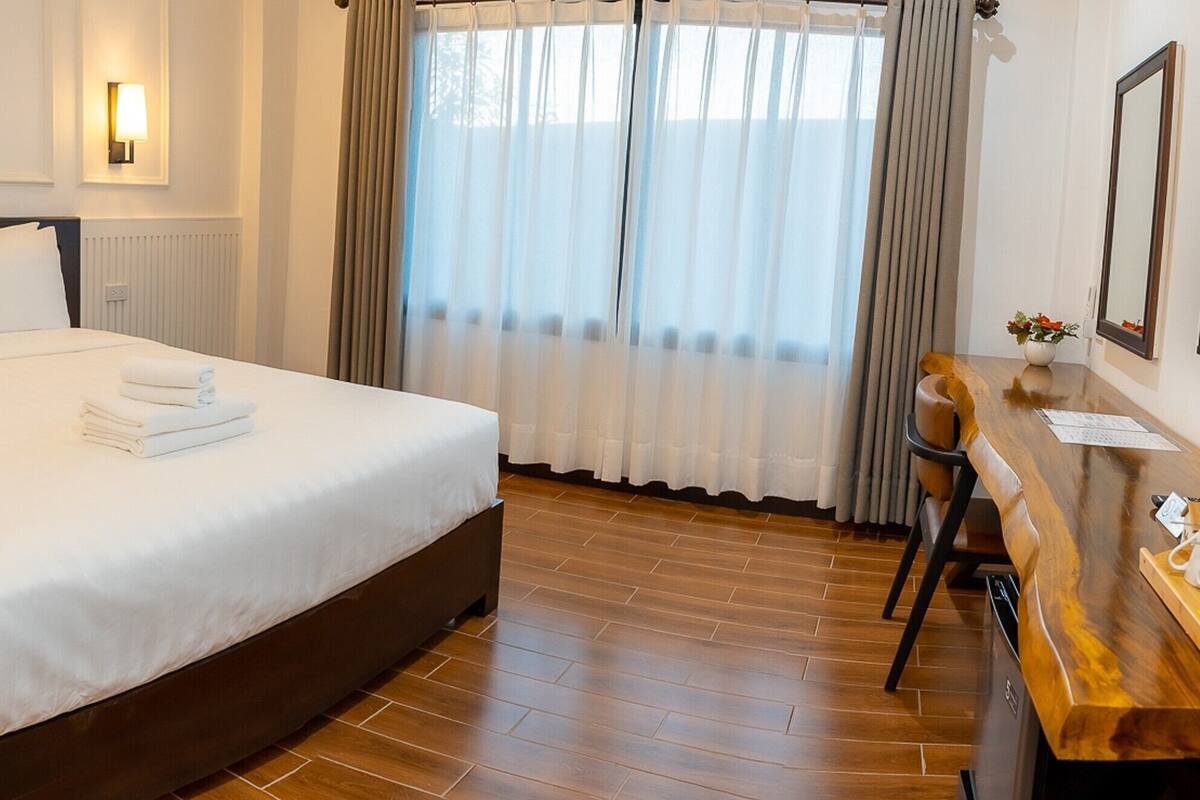 Hotellihuone, jossa on suuri sänky, puinen työpöytä, jossa on vedenkeitin, peili ja ikkuna, jossa on verhot.
