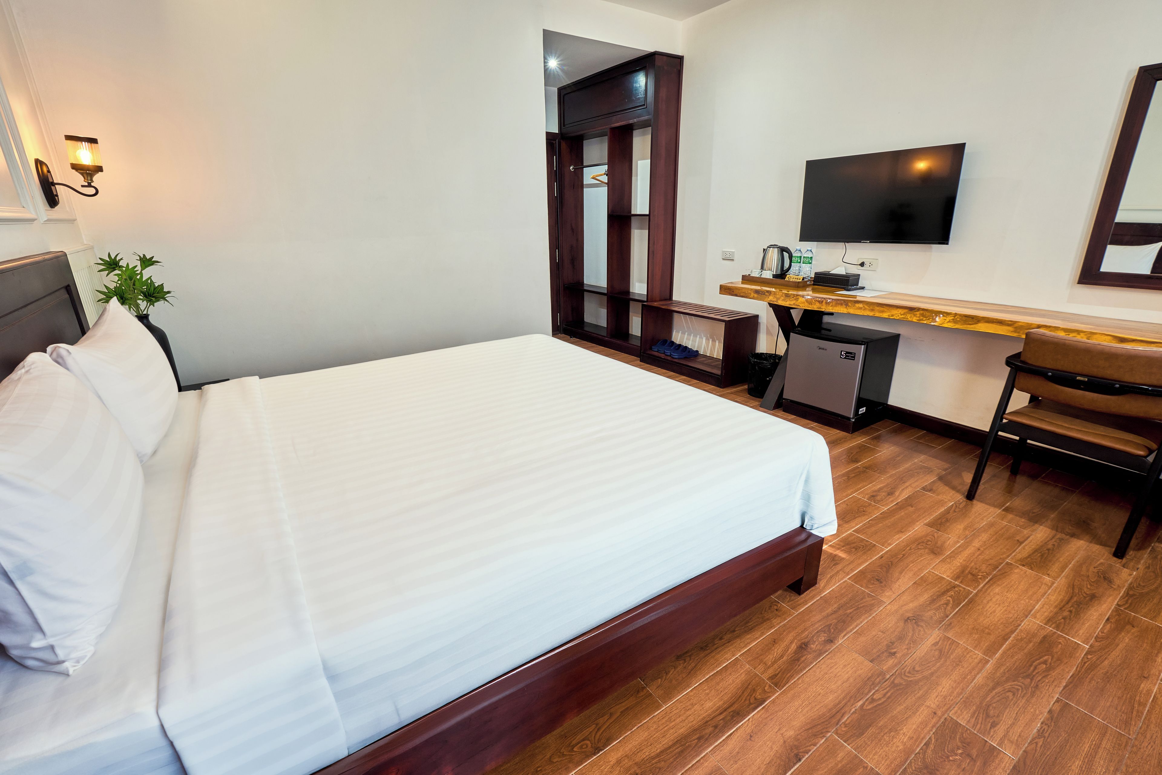 A hotel room with a bed, a desk with a chair, a television, and a small refrigerator.