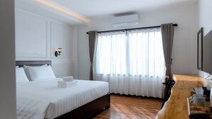 Una habitación de hotel con cama, cómoda de madera, televisor montado en la pared y ventana con cortinas.