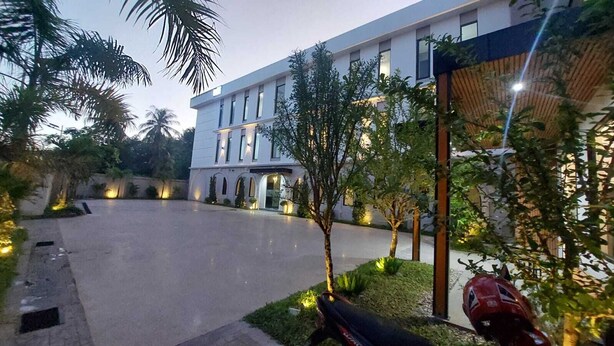 Un edificio moderno con tejado plano, ventanas amplias y un patio empedrado con árboles y un vehículo rojo.