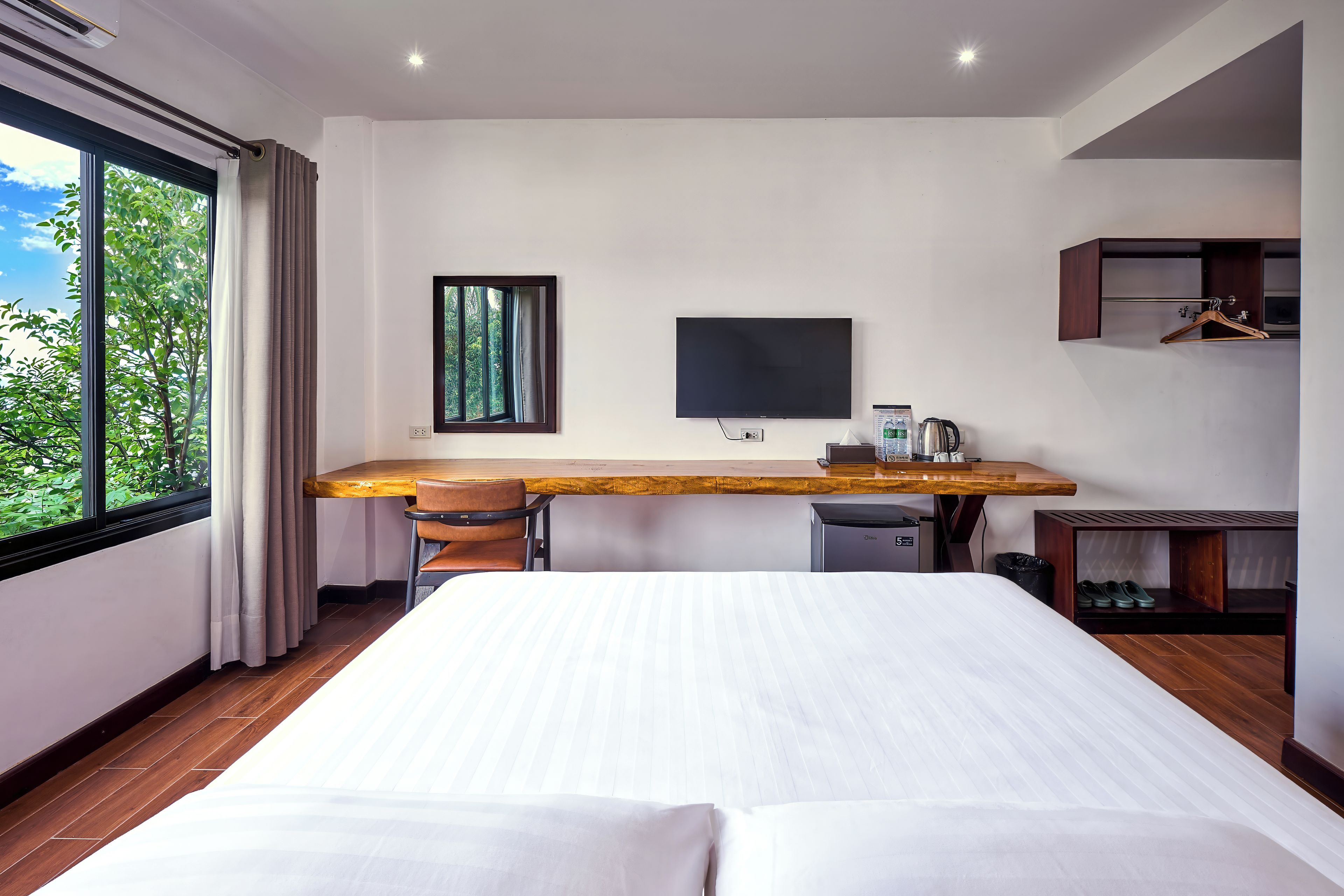 Una habitació d'hotel amb un llit, una taula de treball amb una cadira, un televisor, una cafetera i un armari.