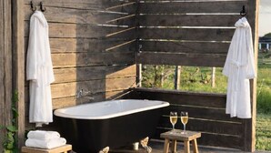 A wooden outdoor bathroom with a bathtub, two wooden stools, and two towels hanging on hooks.