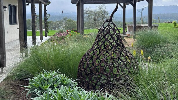 A garden with a metal sculpture, a pergola, and a house with a tiled patio.