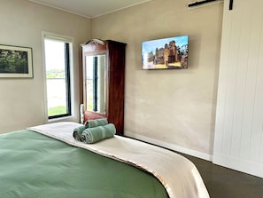 Quarto com cama, janela, porta e quadro na parede.