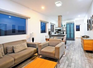 A modern living room with a sofa, armchairs, a coffee table, and a view of the kitchen and dining area. - Gated Community, Oceanview Condo  Pool & Gym (La Paz)