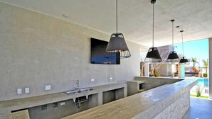 A modern kitchen with a concrete countertop, a sink, pendant lights, and a large window overlooking a pool.