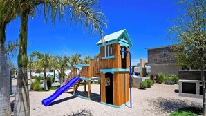 A playground with a slide and climbing structures, surrounded by palm trees and a building labeled 'Hispaniola.'
