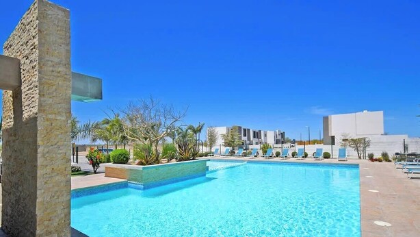 A swimming pool with lounge chairs, a stone pillar, and a modern building in the background.