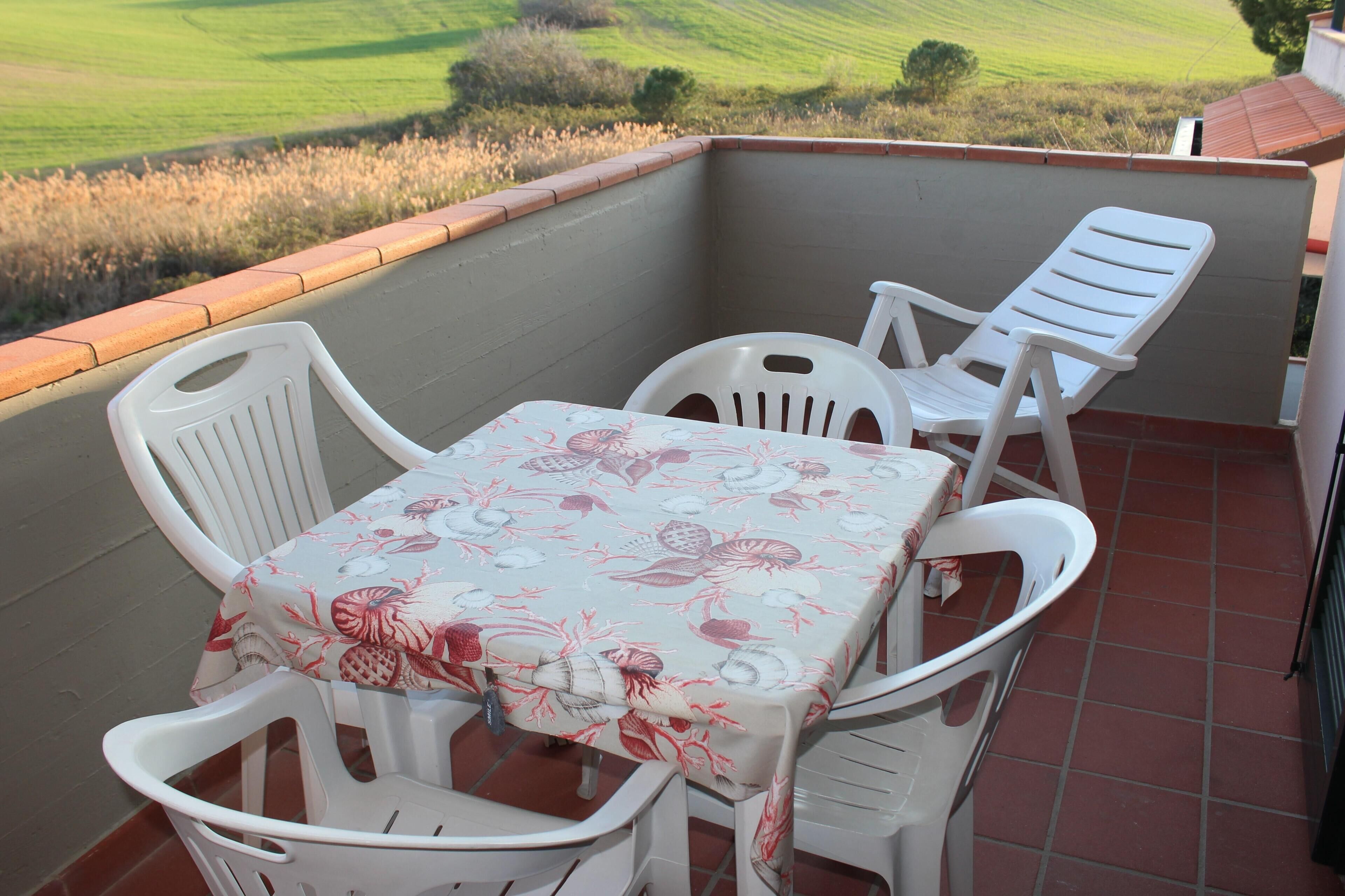A balcony with a table and chairs, a tiled floor, and a view of a green field.
