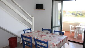 Zona pranzo con tavolo e sedie, televisione a parete e vista attraverso una porta aperta.
