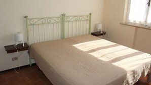 A room with a bed, a nightstand, a lamp, and a window with curtains. - Four-room apartment 30 meters from the sea, with parking space (Marcelli)