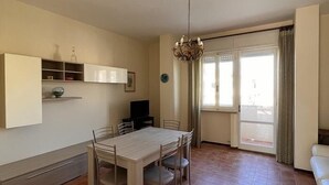 A dining area with a table and chairs, a television, and a window with curtains. - Four-room apartment 30 meters from the sea, with parking space (Marcelli)