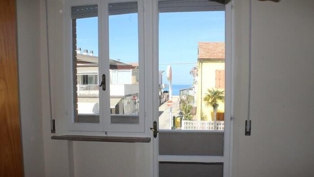 A room with a white door, a small window, and a view of buildings and a flag. - Four-room apartment 30 meters from the sea, with parking space (Marcelli)