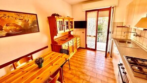 Una cocina con una mesa de madera, armarios, una estufa y un amplio ventanal corredizo que da a un espacio exterior.