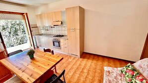 Cocina compacta con comedor, armarios de madera y vista a través de un ventanal.