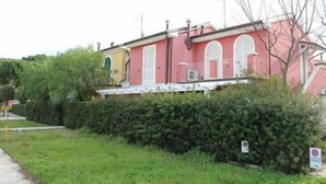 Ein pinkfarbenes Gebäude mit weißen Fensterläden, einem Balkon und einer Hecke davor.