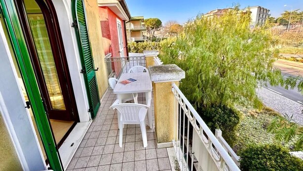 Ein Balkon mit Tisch und Stühlen, einer Tür und Blick auf die Straße und die Häuser.