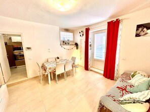 Ein gemütlicher Wohnbereich mit Essplatz, einer Couch und einem Fenster mit roten Vorhängen.