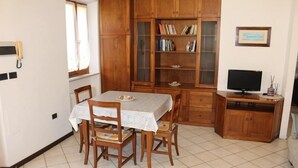 Een eethoek met een tafel, stoelen, een boekenkast, een televisie en een kast.