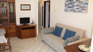 Een woonkamer met een bank, een televisie, een boekenkast en een schilderij.