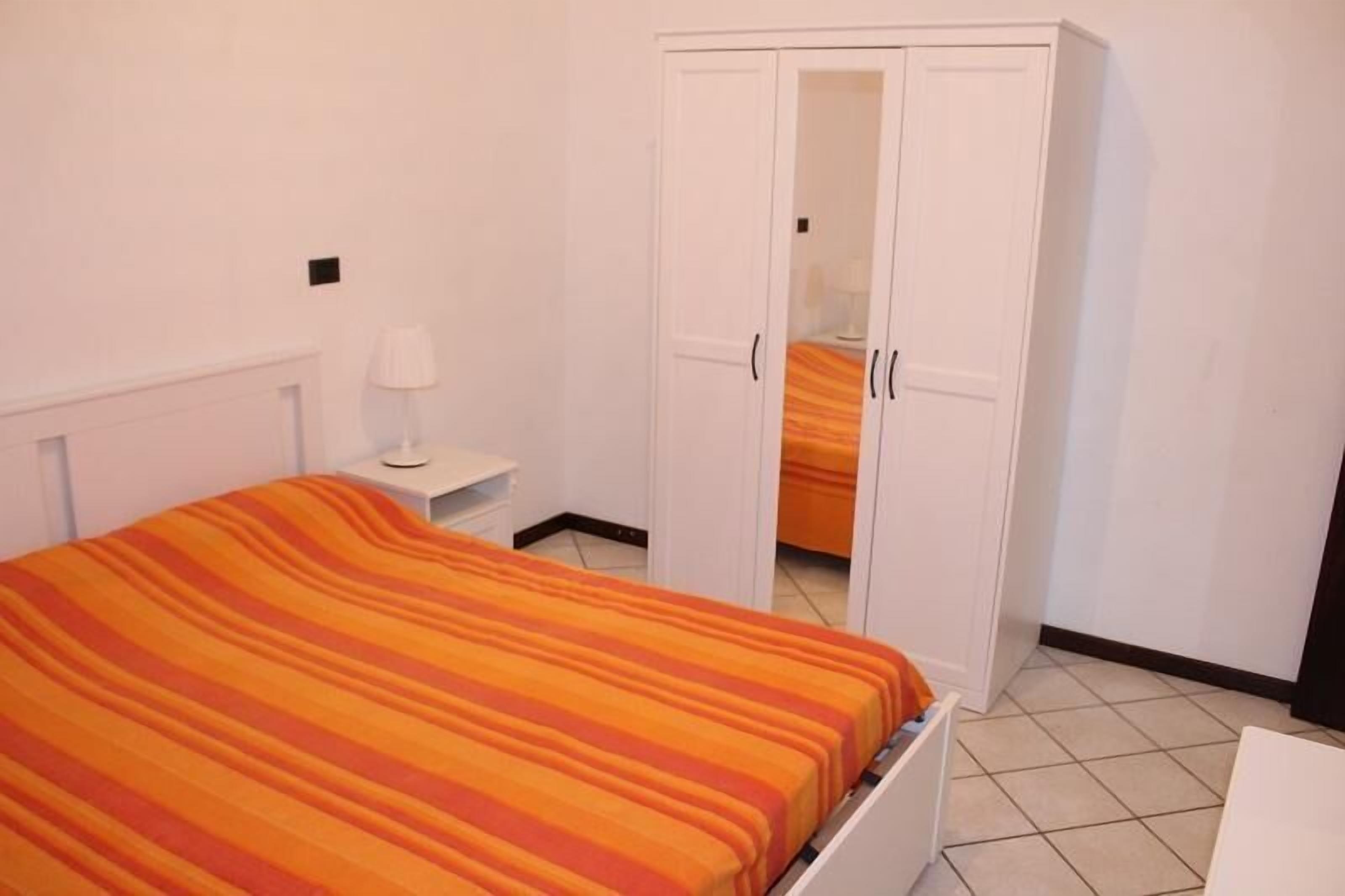Une chambre à coucher comprenant un lit, une table de chevet, une armoire et une salle de bain visible à travers les portes de l’armoire.