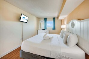 Ein Hotelzimmer mit Bett, einem an der Wand montierten Flachbildfernseher, einem Fenster mit Vorhängen, einem Nachttisch mit Lampe und einem dekorativen Kopfteil.