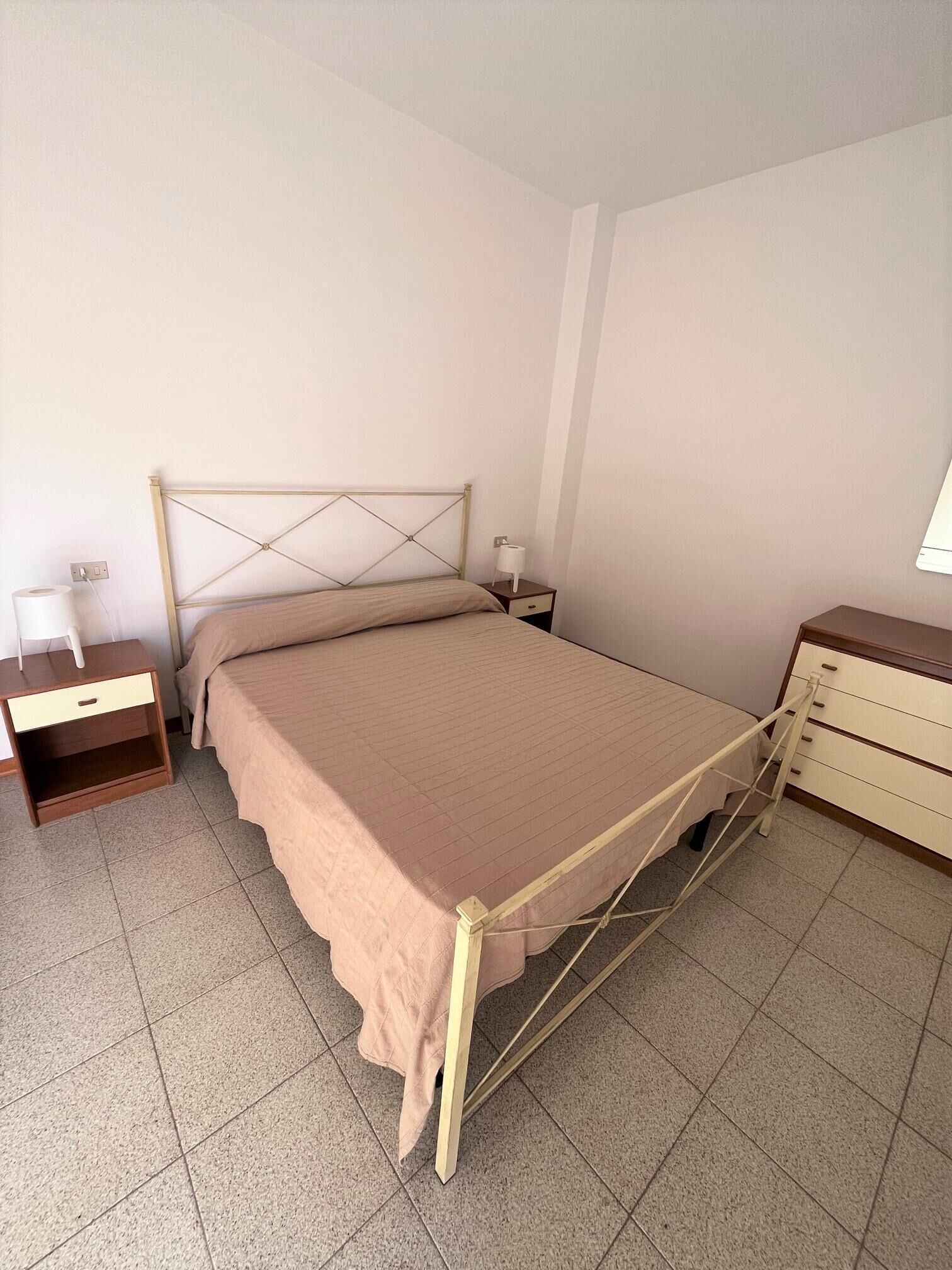 A bedroom with a bed, a nightstand, a dresser, and a wall socket.