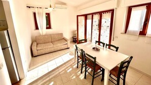 Uma área de refeições com uma mesa e cadeiras, um sofá e uma janela com cortinas.
