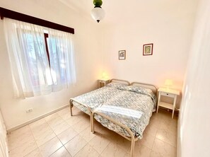Ein Schlafzimmer mit einem Bett, zwei Nachttischen, einem fensterbepflanzten Fenster und einer Deckenleuchte.