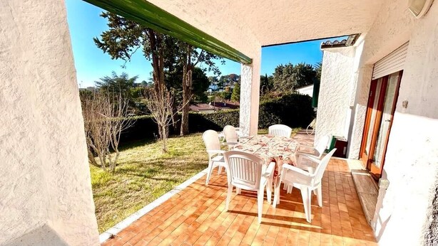 Um pátio com mesa e cadeiras, vista da paisagem circundante e um edifício com fachada branca.