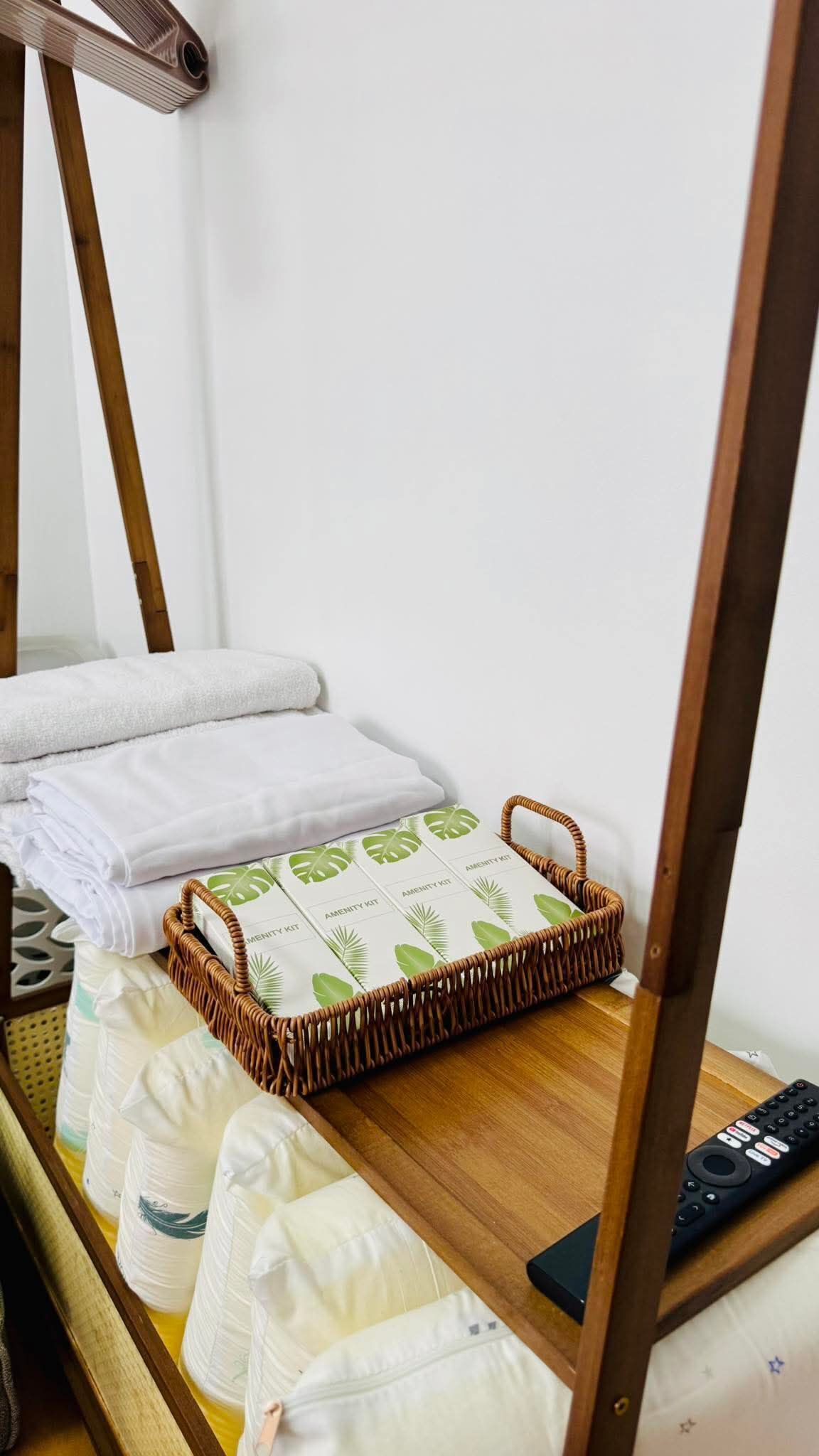 A room with a bed, a remote control, a wicker basket with amenities, and a wooden chair.