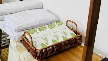 Een kamer met een bed, een afstandsbediening, een rieten mand met toiletartikelen en een houten stoel.