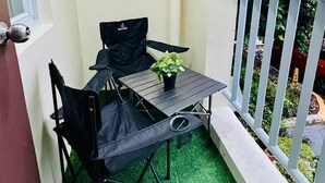 Uma varanda com uma pequena mesa, duas cadeiras, um vaso de planta e guarda-corrimão branco.
