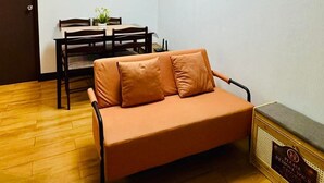 Quarto com piso de madeira, sofá, mesa de jantar com cadeiras e luminária no teto.