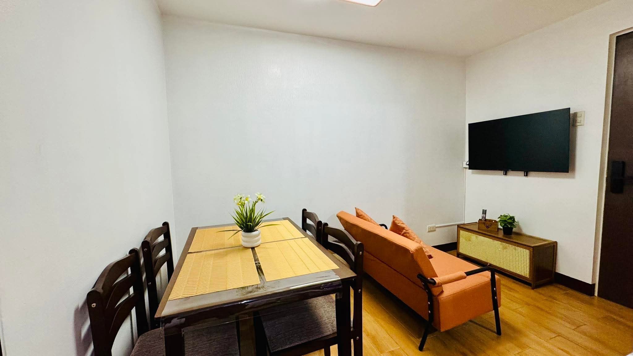 Un espace repas comprenant une table, des chaises, un banc, une plante en pot, un téléviseur et un petit meuble.