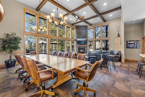 Un comedor amplio con una gran mesa de madera y sillas de cuero, rodeado de ventanas que ofrecen vistas a árboles.
