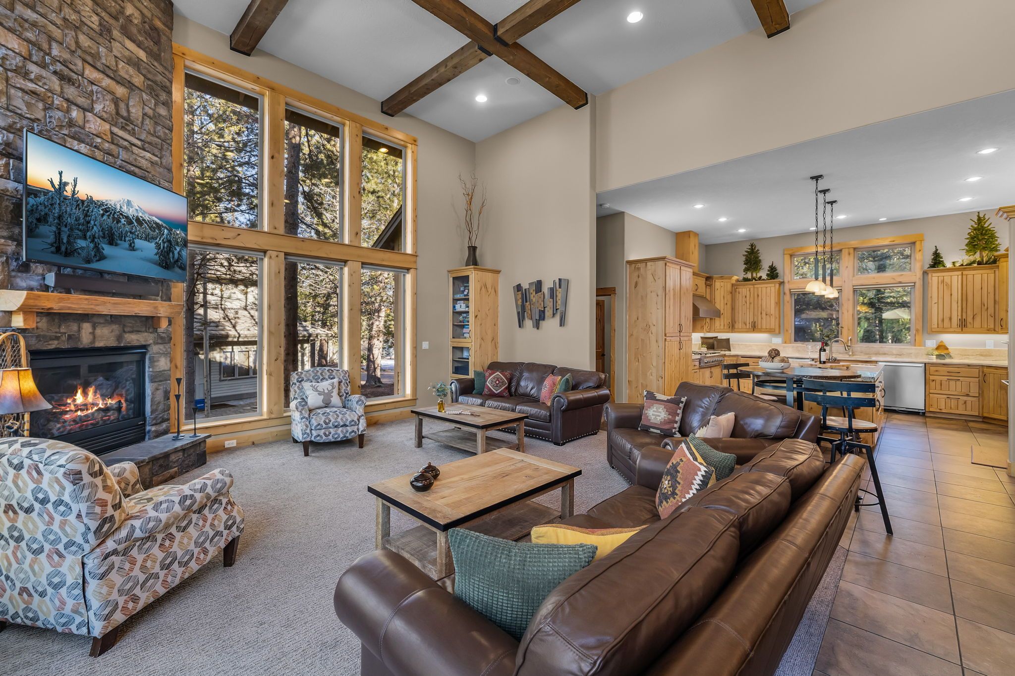 A spacious living room with a fireplace, leather sofas, a coffee table, and a large window offering a view of trees.