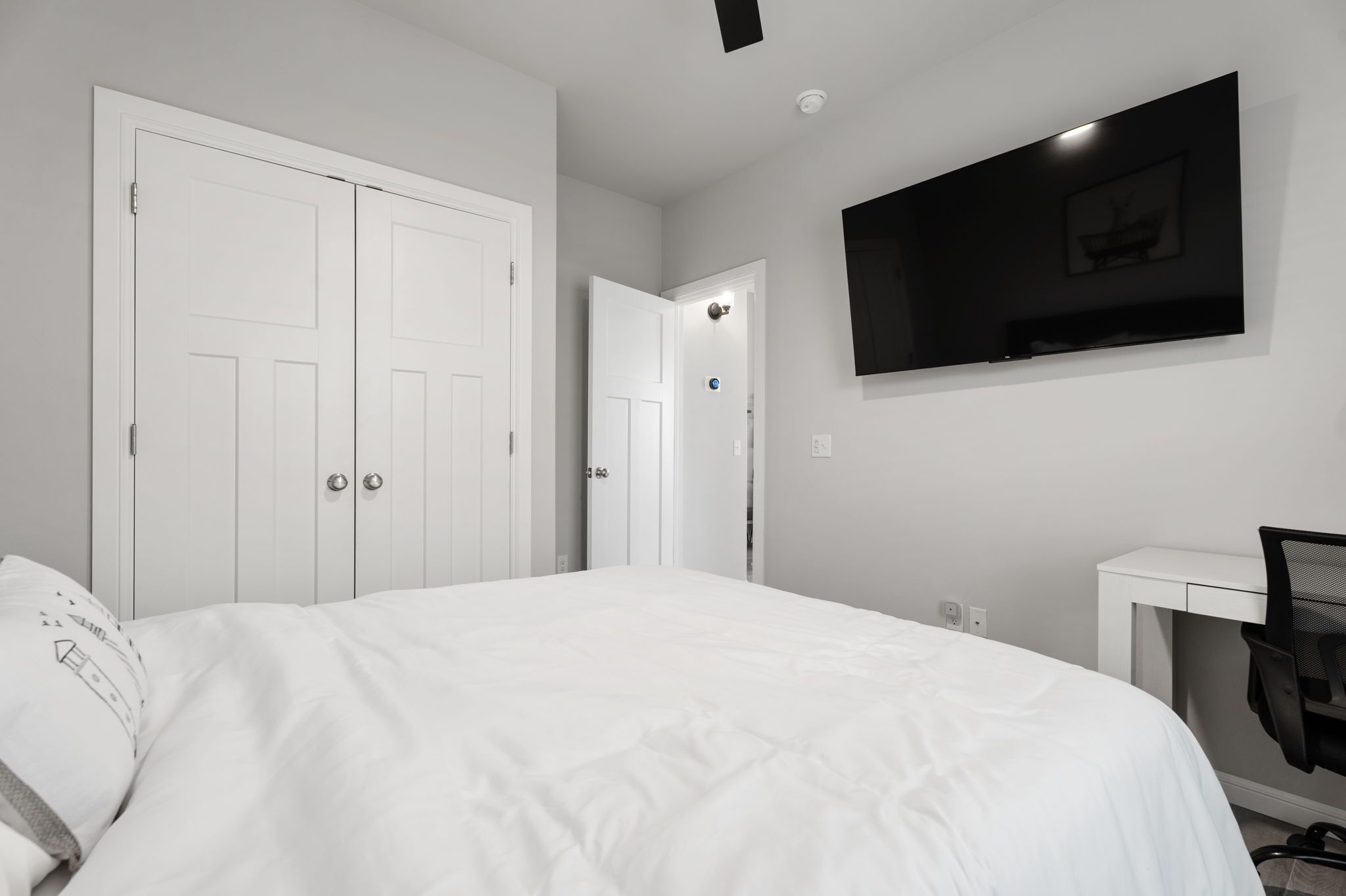 Une chambre à coucher avec un lit, un bureau, une chaise, un téléviseur et deux portes.
