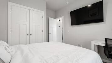 Une chambre à coucher avec un lit, un bureau, une chaise, un téléviseur et deux portes.