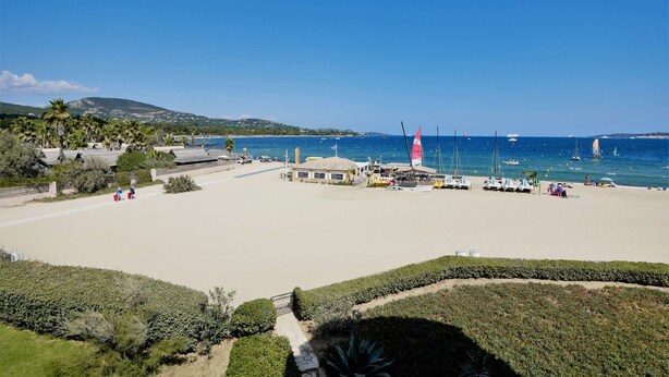 Una spiaggia con cielo sereno, palme e barche nell'acqua.