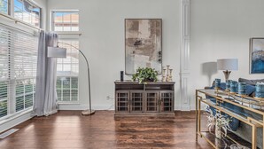 A room with a wooden floor, a console table with a plant, a large abstract painting, and a sofa with decorative items. - Centrally Located Retreat (Indianapolis)