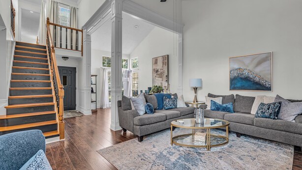 A spacious living room with a grey sofa, a round coffee table, and a staircase leading to an upper level. - Centrally Located Retreat (Indianapolis)