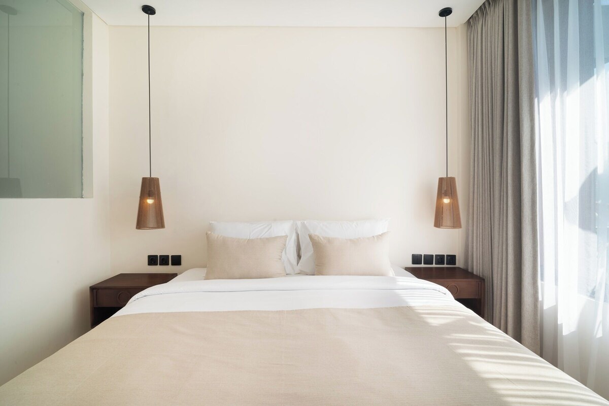 A modern hotel room with a large bed, two bedside tables, and pendant lighting.