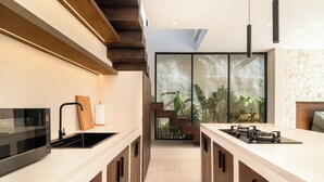 A modern kitchen with a central island, a built-in microwave, and a large window overlooking a garden. - La Finca Villa Bingin, Uluwatu by Sandara (Pecatu)