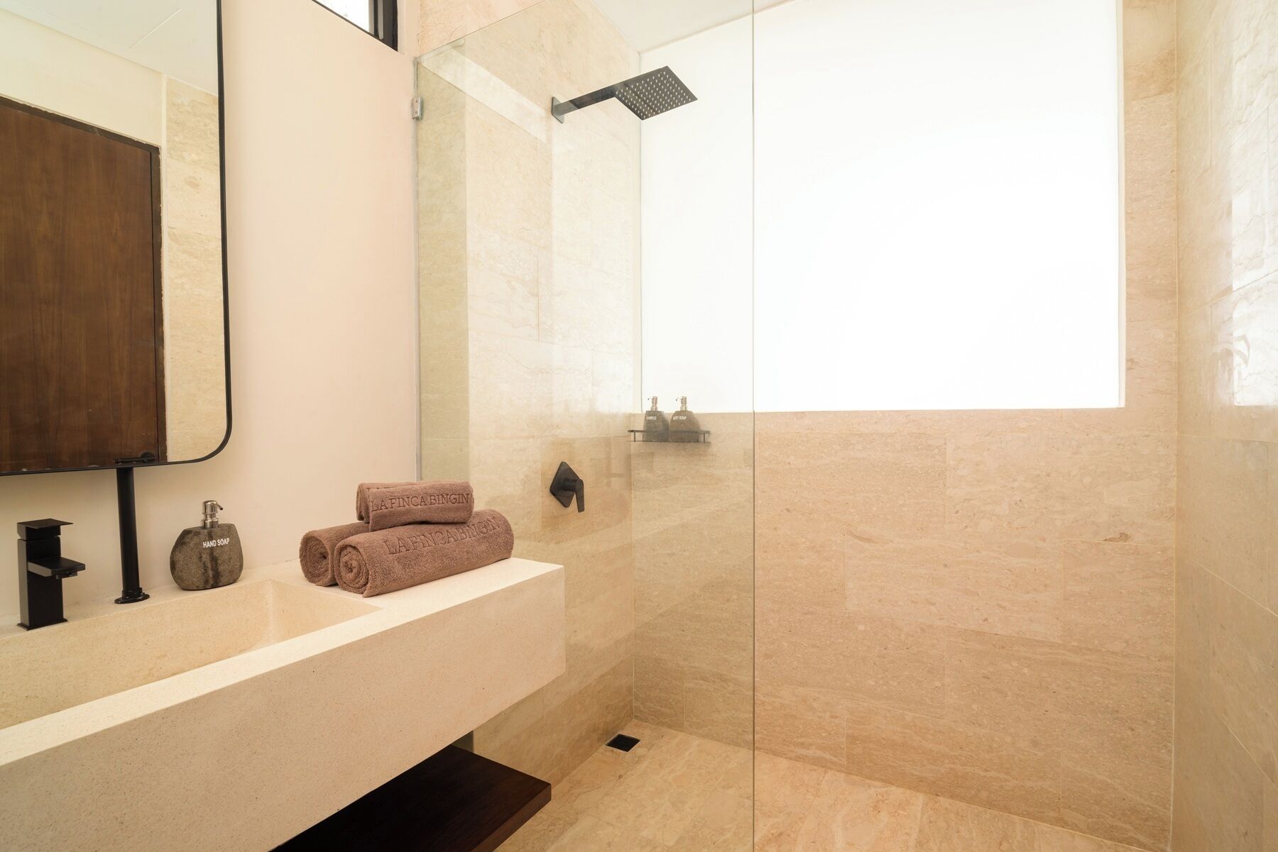 A modern bathroom with a glass shower enclosure, a vanity with a mirror, and two hand soap dispensers.