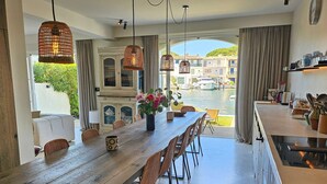 Un espace repas avec une longue table en bois, des chaises en osier et des lampes en osier suspendues au plafond.